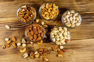Ahşap masada fındık çeşitleri. Badem, fındık, şam fıstığı, ceviz ve cam kaselerde ceviz. Üst Manzara. Sağlıklı yeme kavramı