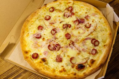 Tahta bir masanın üzerindeki karton kutuda nefis taze pizza. Yemek teslimatı, fast food, pizza teslimatı.