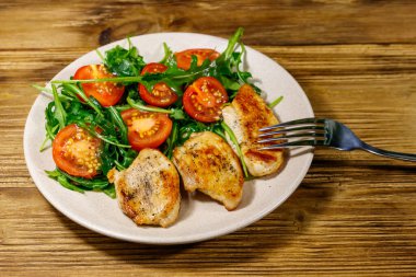 Kızarmış tavuk göğsü, taze roka salatası ve ahşap masada vişneli domates.