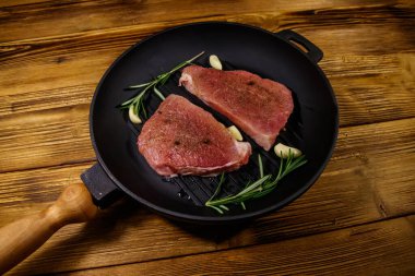 Biberiye, sarımsak ve baharatlı çiğ domuz bifteği ahşap masada ızgara demir tavada pişirilmeye hazır.