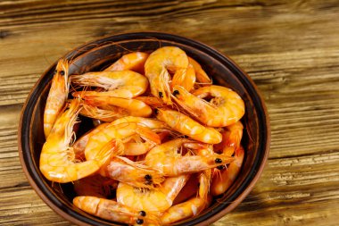 Tahta masadaki seramik kasede taze çiğ karidesler.