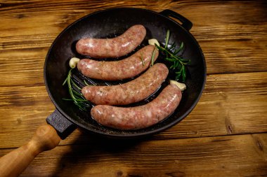 Çiğ sosisler hazır biberiye, sarımsak ve baharatlarla ahşap masada ızgara ızgara demir tavada.
