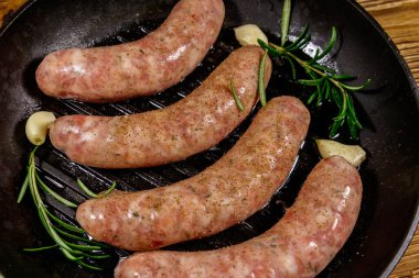 Çiğ sosisler, biberiye, sarımsak ve baharatlı ızgara ızgara tavada hazır.