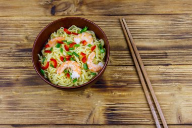 Bir kase karidesli Çin eriştesi, yeşil soğan ve ahşap masada kırmızı acı biber. Üst görünüm