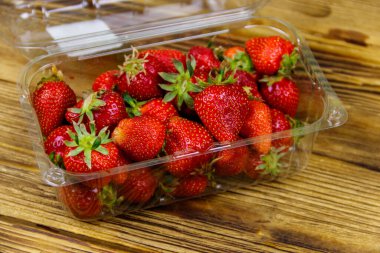 Tahta bir masada plastik kutuda taze çilek.