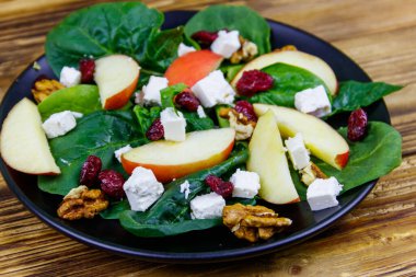 Elmalı ıspanak salatası, feta peyniri, ceviz ve ahşap masada kurutulmuş kızılcık. Sağlıklı vejetaryen yemekleri