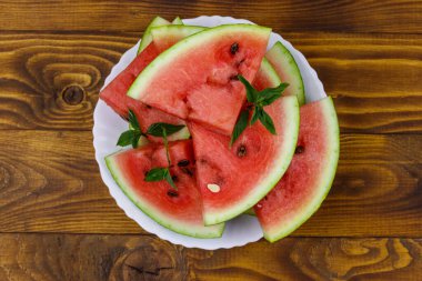 Tahta bir masanın üzerinde beyaz tabakta taze olgun dilimlenmiş karpuz. Üst görünüm