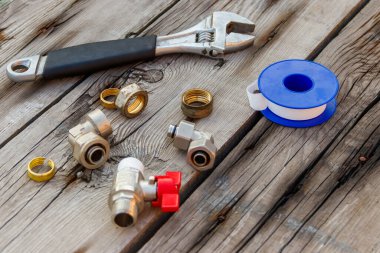 Çeşitli tesisat yedek parçaları, bant mühürleme ve ahşap arka planda ayarlanabilir ingiliz anahtarı.