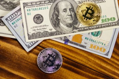 Altın ve gümüş paralar ve 100 dolarlık banknotlar ahşap masada.