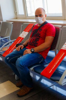 Tıbbi maske takan ve havaalanında uçuş için bekleyen bir adam. Pandemik ve kişisel koruma süresince seyahat kavramı