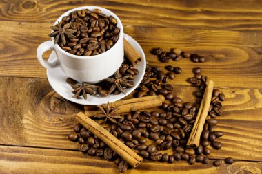 Beyaz fincanda kahve çekirdekleri, tarçın çubukları ve ahşap masada yıldız anason.