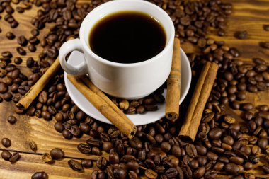 Bir fincan kahve, kavrulmuş kahve çekirdekleri ve ahşap masada tarçın çubukları.