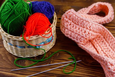 Hasır sepet, renkli örgü iplikleri, örgü iğneleri ve ahşap masa üzerine örülmüş eşarp.