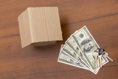 Küçük karton ev, anahtarlar ve paralar ahşap masada. Kredi, ev kredisi. Konut satın alma. Emlak sigortası. Konutun kirası