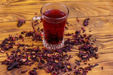 Ahşap masada bir bardak kırmızı amber çayı (carcade, roselle).