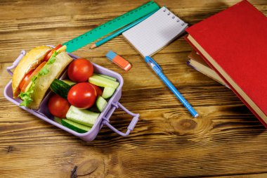 Okul konseptine geri dönelim. Okul malzemeleri, kitaplar, hamburgerler ve ahşap bir masada taze sebzeler.