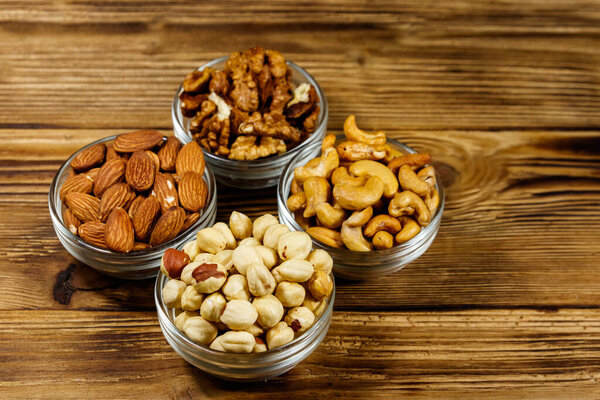 Assortment of nuts on wooden table. Almond, hazelnut, walnut and cashew in glass bowls. Healthy eating concept