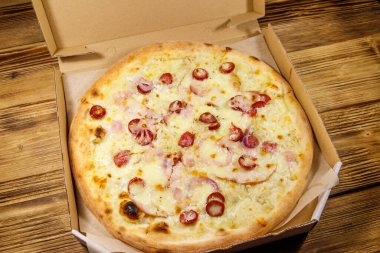 Tahta bir masanın üzerindeki karton kutuda nefis taze pizza. Yemek teslimatı, fast food, pizza teslimatı.