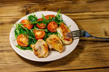 Kızarmış tavuk göğsü, taze roka salatası ve ahşap masada vişneli domates.