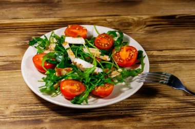 Lezzetli tavuk göğsü salatası, taze roka ve ahşap masada kiraz domatesleri.