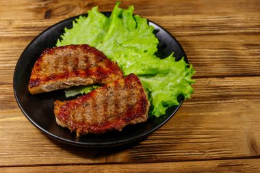 Ahşap masada marul yapraklı ızgara domuz bifteği.