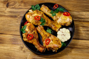 Ahşap bir masada siyah tabakta baharatlı kızarmış tavuk budu. Üst görünüm