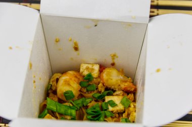 Kızarmış pirinç eriştesi, karidesli Pad Thai ve açık karton pakette tofu. Tayland mutfağı, yemek teslimatı.