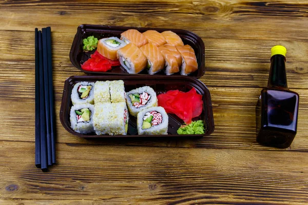 Set of sushi rolls in plastic boxes, soy sauce and chopsticks on wooden table. Sushi for take away or delivery of sushi in plastic containers