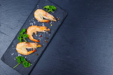 Siyah zemin üzerinde maydanozlu, tuzlu ve biberli büyük çiğ karidesler. Üst görünüm, alanı kopyala