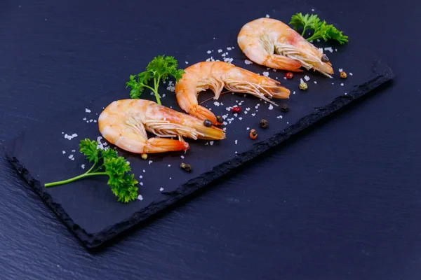 Siyah arkaplanda maydanozlu, tuzlu ve biberli büyük çiğ karidesler.