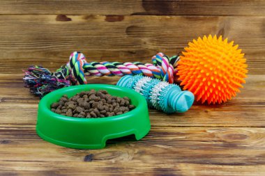 Köpek oyuncakları ve ahşap arka planda yeşil plastik kasedeki köpekler için yem. Köpek bakımı kavramı