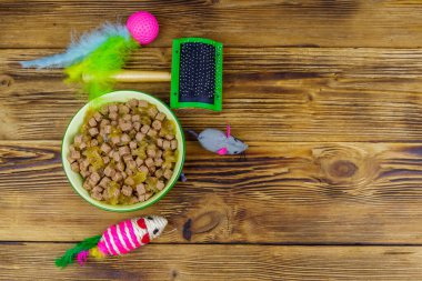 Kasede konserve kedi maması, kedi oyuncakları ve ahşap arka planda evcil hayvan fırçası. Üst görünüm, boşluğu kopyala. Hayvan bakımı konsepti