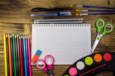 Okul Kırtasiye malzemeleri kümesi. Boş defter, kalem, kalem, suluboya boyalar, makas, Boya fırçaları, silgi ahşap masa üzerinde renkli. Geri okul kavramı