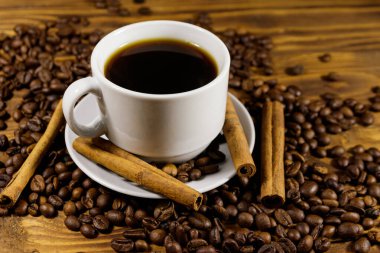 Bir fincan kahve, kavrulmuş kahve çekirdekleri ve ahşap masada tarçın çubukları.