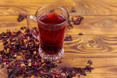 Ahşap masada bir bardak kırmızı amber çayı (carcade, roselle).
