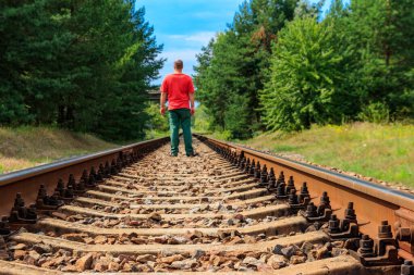 Yalnız adam tren yolunda yürüyor.