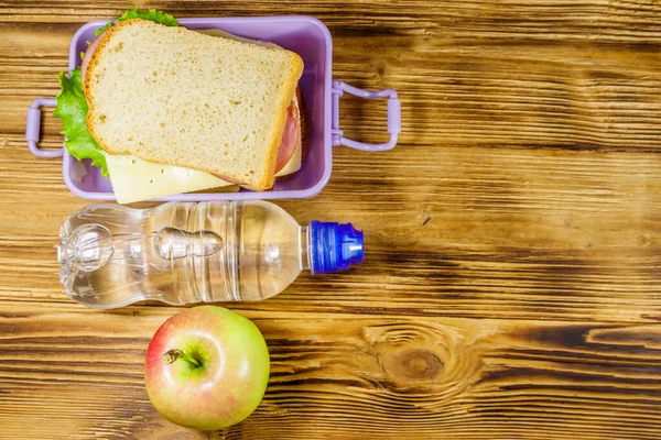 Sandviçli beslenme çantası, ahşap bir masada bir şişe su ve elma. Üst görünüm, alanı kopyala