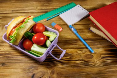 Okul konseptine geri dönelim. Okul malzemeleri, kitaplar, hamburgerler ve ahşap bir masada taze sebzeler.