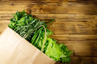 Yeşil soğanlı kağıt torbası, biberiye, marul yaprakları ve ahşap masada maydanoz. Üst Manzara. Sağlıklı gıda ve market alışverişi kavramı