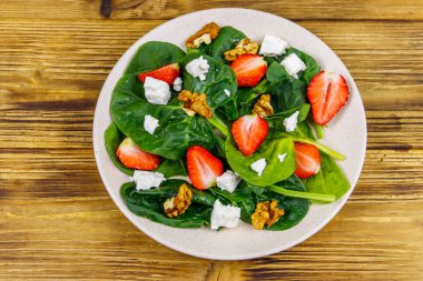 Çilekli, ıspanaklı, cevizli ve ahşap masadaki peynirli taze sağlıklı salata. Üst görünüm