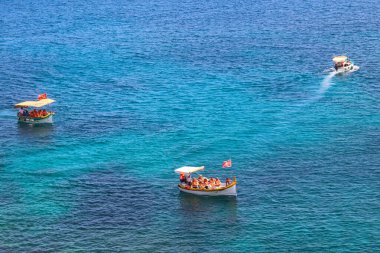 Marsaxlokk, Malta - 18 Mayıs 2025: Geleneksel luzzu teknesiyle seyahat eden turistler ve Malta 'nın en güzel doğal yüzme havuzlarından biri olan Aziz Peter Havuzu' nun güzel manzarasının keyfini çıkarıyorlar