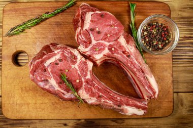 Kemiğin üzerinde çiğ biftek, baharatlar ve ahşap masada biberiye. Üst görünüm