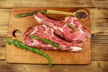 Kemiğin üzerinde çiğ biftek, baharatlar ve ahşap masada biberiye. Üst görünüm