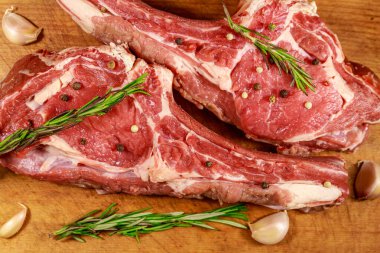 Baharat, sarımsak ve biberiye ahşap masada kemik çiğ taze sığır kaburga göz biftek. Üstte görüntü