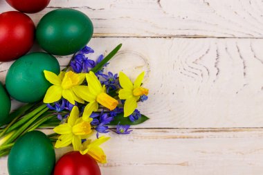 Boyanmış Paskalya yumurtaları, sarı nergis buketi ve beyaz ahşap arka planda mavi scilla çiçekleri. Paskalya kompozisyonu. Üst görünüm, alanı kopyala