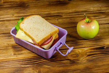 Tahta bir masada, sandviç ve elmayla beslenme çantası.