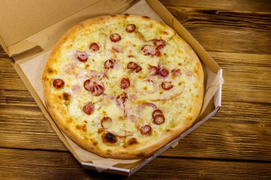 Tahta bir masanın üzerindeki karton kutuda nefis taze pizza. Üst Manzara. Yemek teslimatı, fast food, pizza teslimatı.