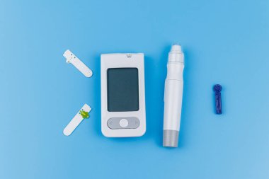 Dijital glukometre, tükenmez kalem, tek kullanımlık iğneler ve pastel mavi arka planda test şeritleri. Üst Manzara. Diyabet kavramı