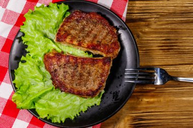 Ahşap masada marul yapraklı ızgara domuz bifteği. Üst görünüm