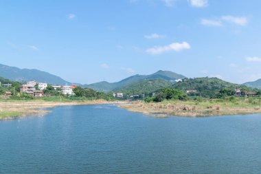 Mavi gökyüzü, yeşil dağlar ve gölün etrafındaki ağaçlar